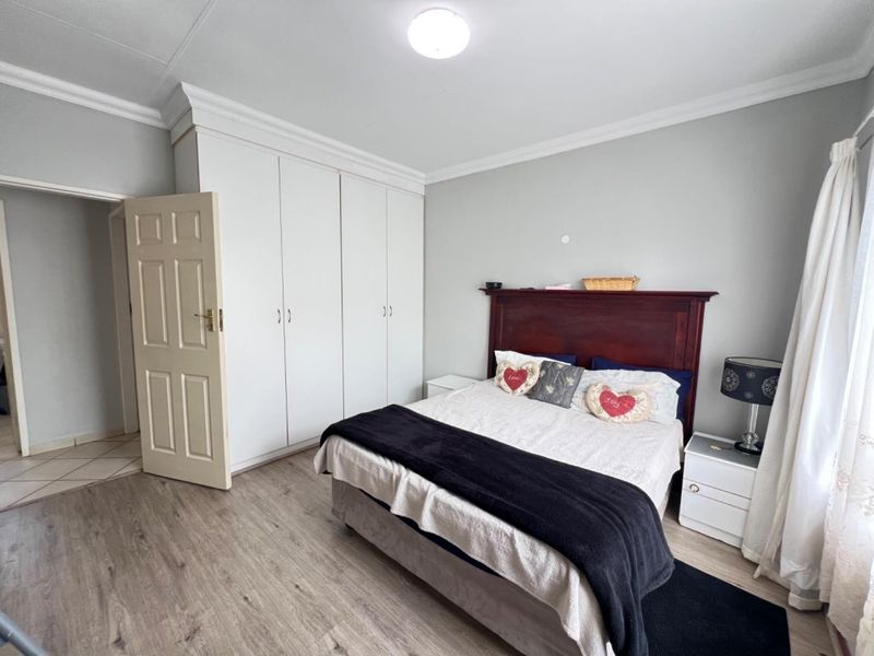 A well-maintained bedroom featuring light-toned laminate flooring, neutral walls, and ample built-in cupboard storage.