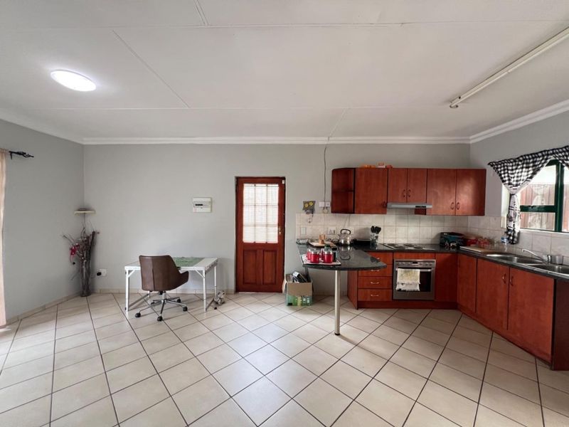 Open-plan kitchen and living area featuring wooden cabinetry, granite countertops, built-in oven, hob, and tiled flooring throughout.