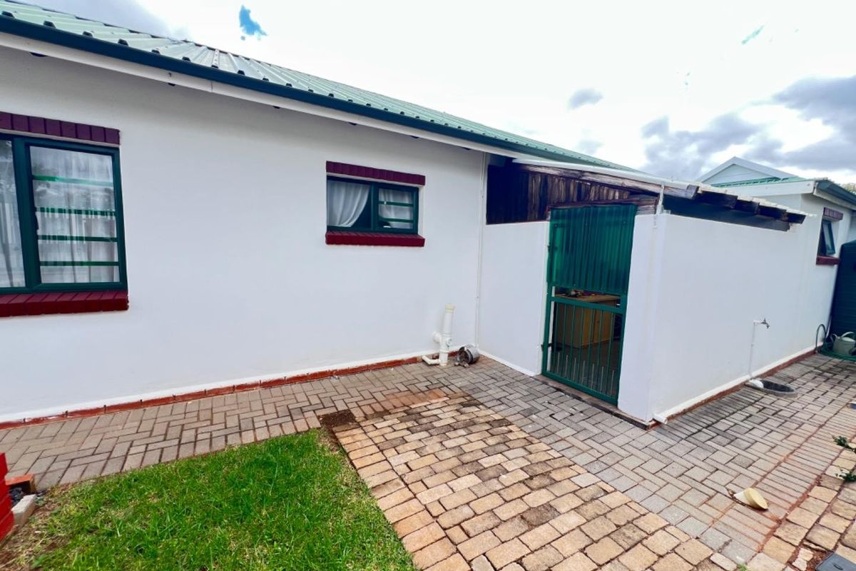 Rear exterior view of the townhouse featuring a paved walkway, small lawn area, and a secure gated entrance.