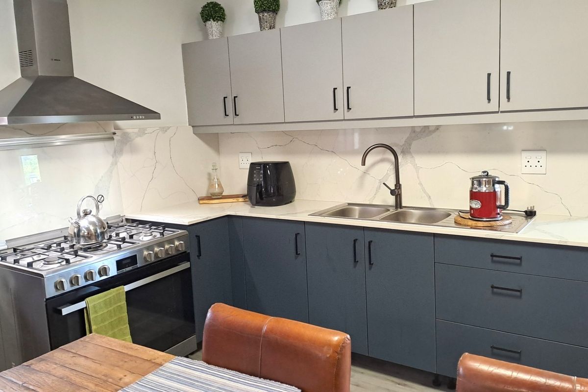 Modern kitchen featuring dark grey lower cabinetry, light grey upper cabinets, quartz countertops, marble-look splashback, and a stainless steel gas stove with extractor.