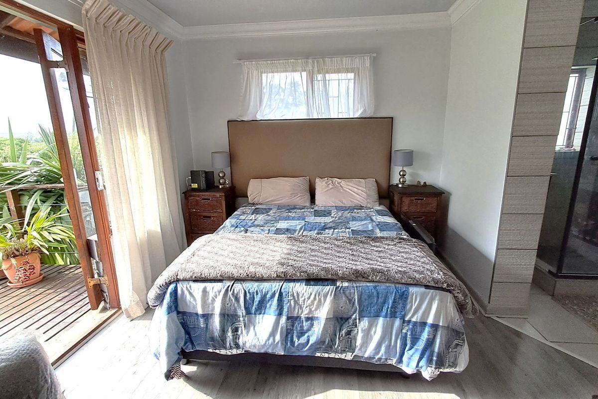 A well-lit bedroom featuring laminate flooring, crown molding, and a sliding glass door leading to a private wooden deck, with an attached en-suite shower.