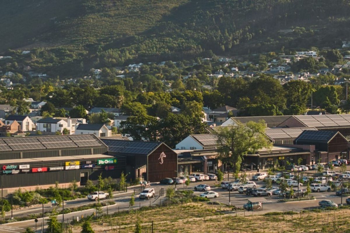 An aerial view of a modern commercial shopping complex featuring solar panels, extensive parking, and surrounding residential landscape.