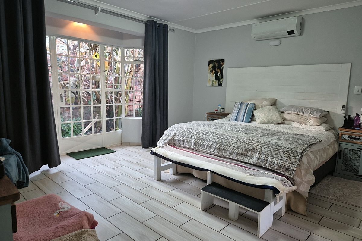 Spacious bedroom featuring light-toned tiled flooring, a wall-mounted air conditioning unit, and large French doors providing natural light and garden access.