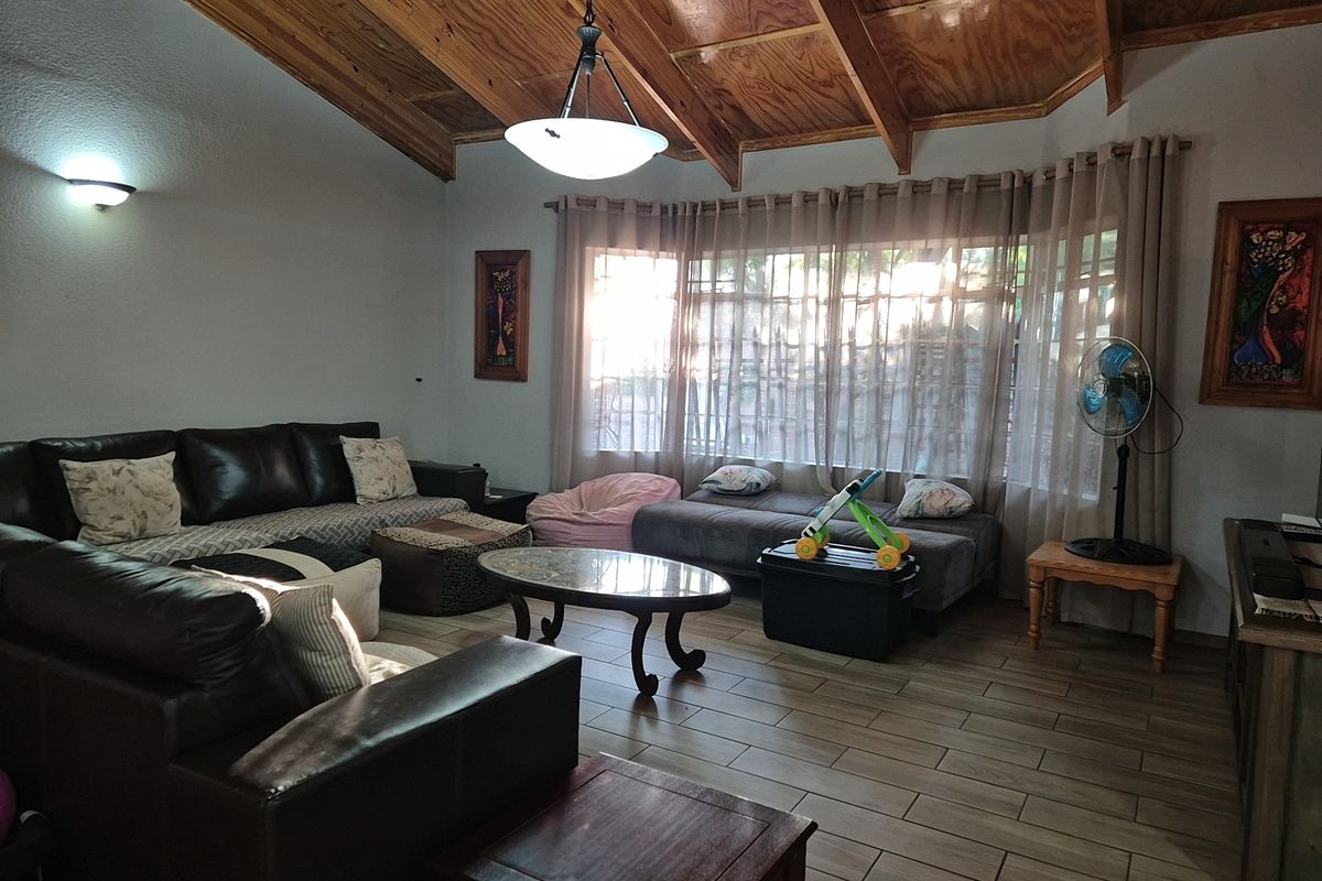 Spacious living room featuring a vaulted timber ceiling with exposed beams, ceramic tile flooring, and a large bay window providing natural light.