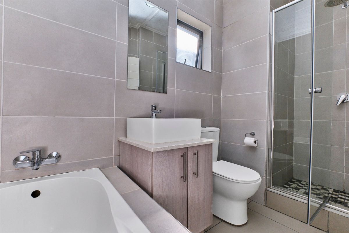 Modern bathroom featuring a built-in vanity with vessel sink, separate bathtub, and a glass-enclosed shower with neutral wall and floor tiling.