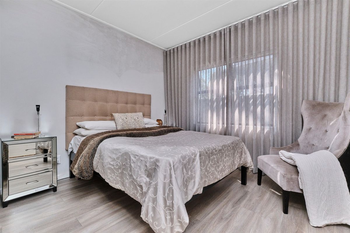 A well-lit bedroom featuring light-toned laminate flooring and floor-to-ceiling window treatments.