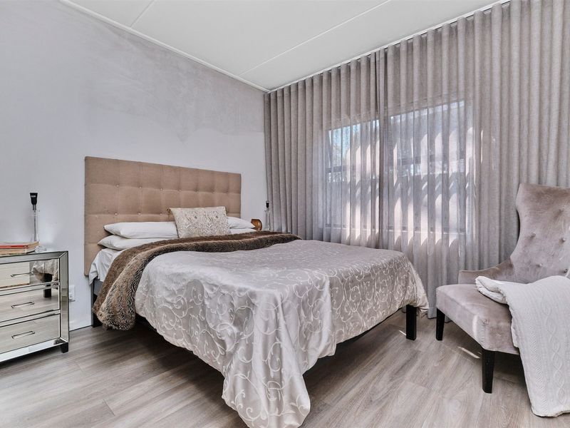 A well-lit bedroom featuring light-toned laminate flooring and floor-to-ceiling window treatments.