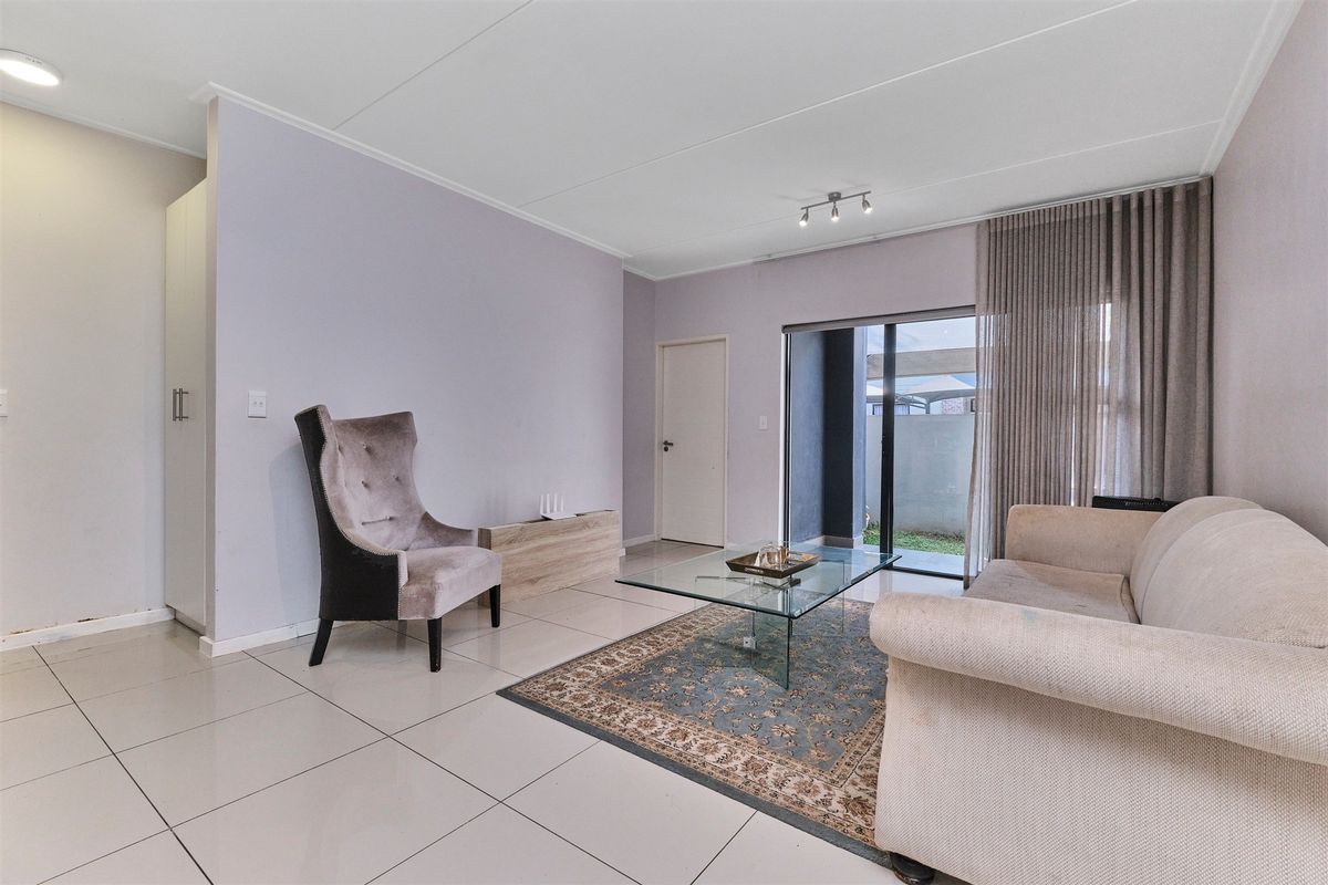 A bright living room featuring large format floor tiles, neutral walls, and a sliding glass door providing access to the outdoor area.