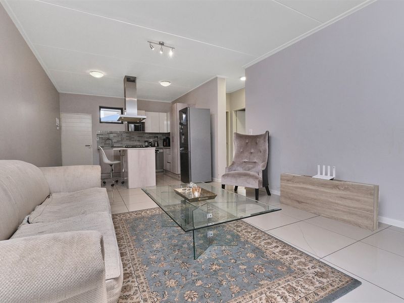 An open-plan living and kitchen area featuring tiled flooring, modern cabinetry, and a central kitchen island with a stainless steel extractor fan.