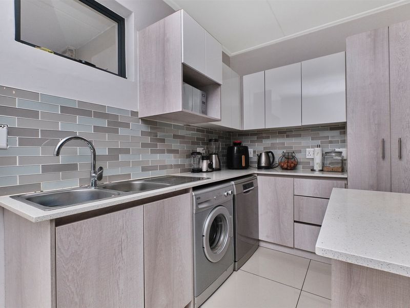 Modern kitchen featuring light wood-grain cabinetry, stone countertops, a stylish subway tile backsplash, and integrated appliances including a dishwasher and washing machine.