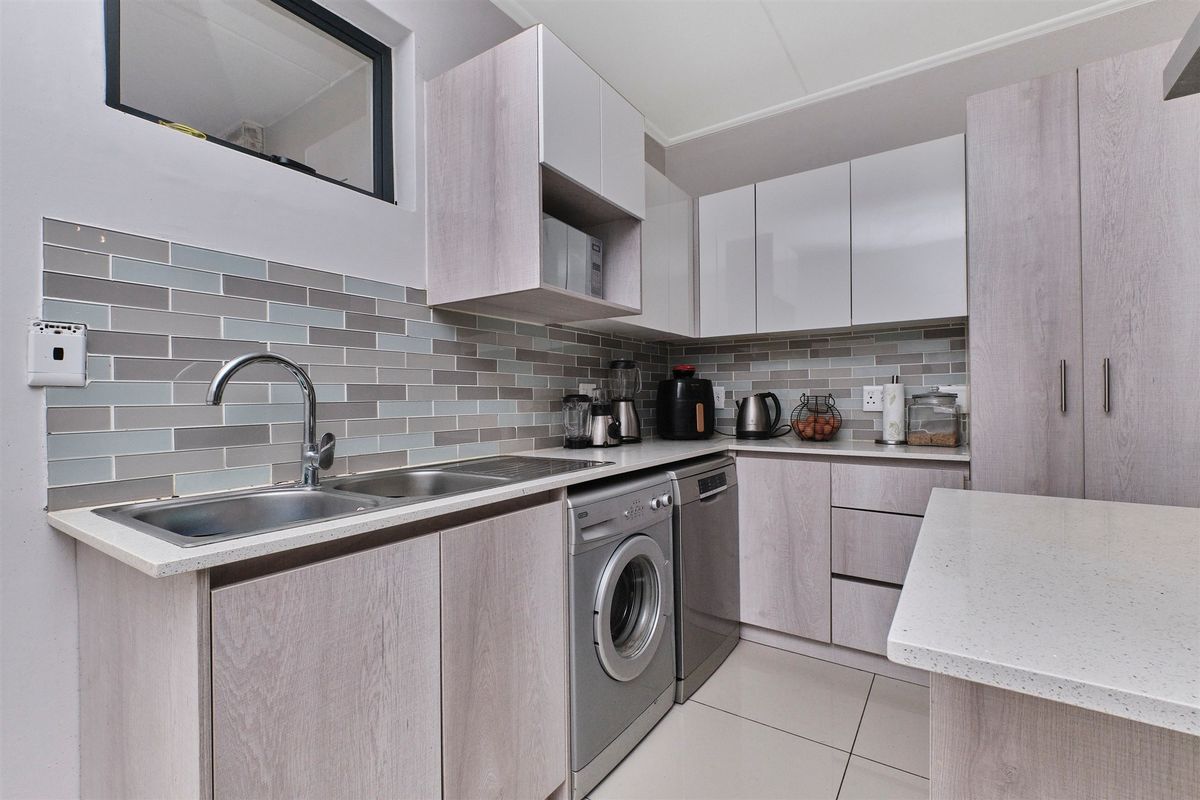 Modern kitchen featuring light wood-grain cabinetry, stone countertops, a stylish subway tile backsplash, and integrated appliances including a dishwasher and washing machine.