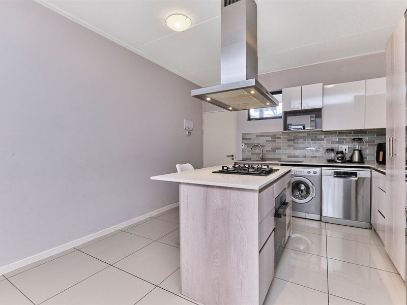 Modern kitchen featuring a central island with a gas hob, stainless steel extractor, tiled flooring, and sleek built-in cabinetry with integrated appliances.