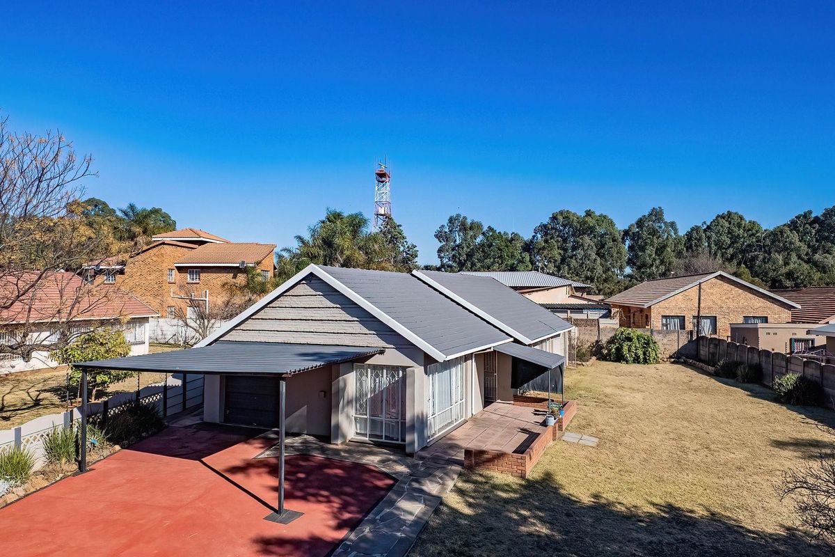 Aerial view of a residential property featuring a tiled roof, attached carport, paved driveway, and a brick patio area within a fenced yard.