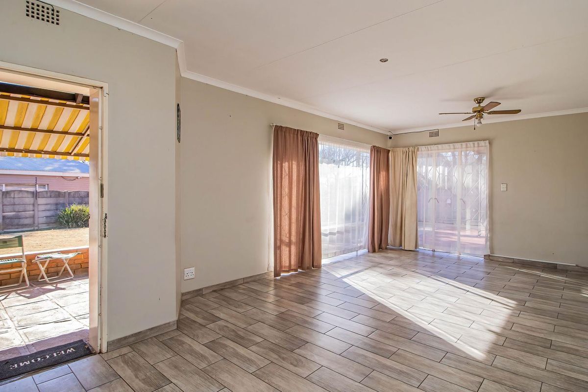 Spacious, light-filled living area featuring neutral tiled flooring, a ceiling fan, and large sliding glass doors providing direct access to the outdoor patio.
