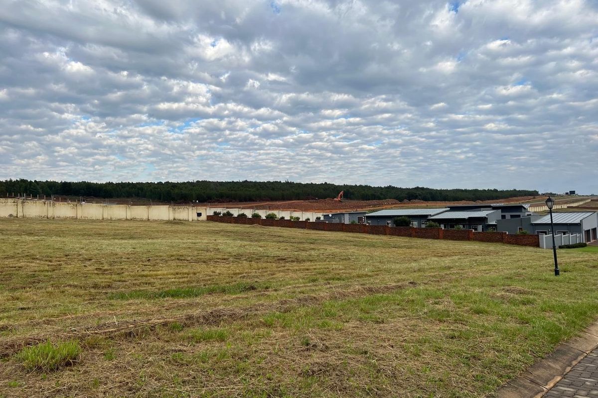 A vacant residential plot featuring a level grass surface, enclosed by perimeter boundary walls, situated within a developed estate setting.