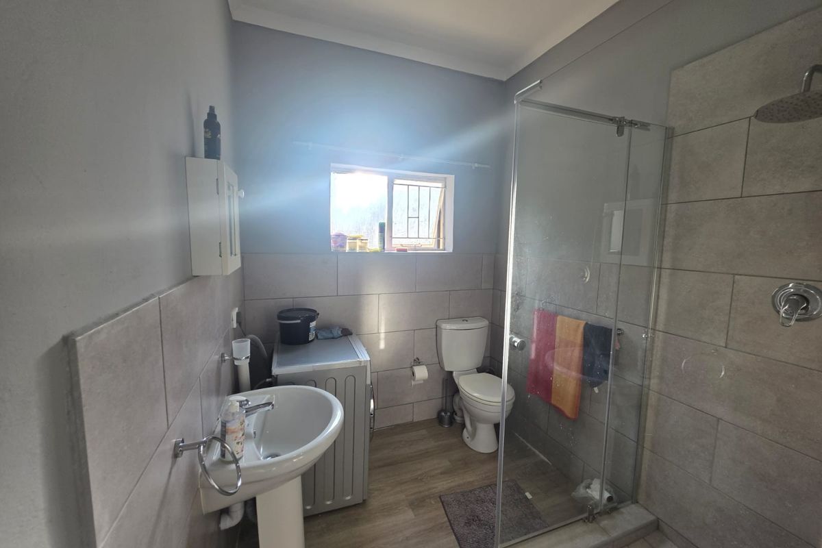 A functional bathroom featuring a pedestal basin, toilet, and a modern glass-enclosed shower with tiled finishes.