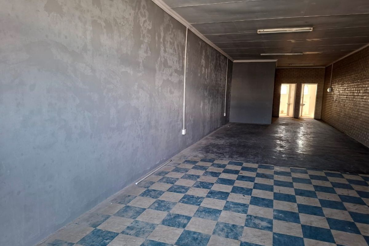 An empty, open-plan commercial space featuring checkered flooring, exposed brickwork, and basic fluorescent lighting, suitable for various retail or office configurations.