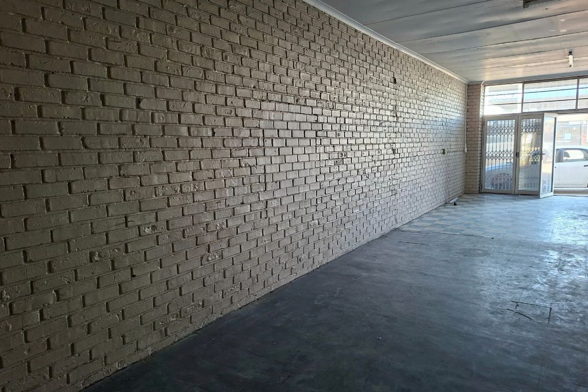 An empty commercial utility space featuring painted brick walls, concrete flooring, and a secure entrance gate, suitable for various business or storage applications.
