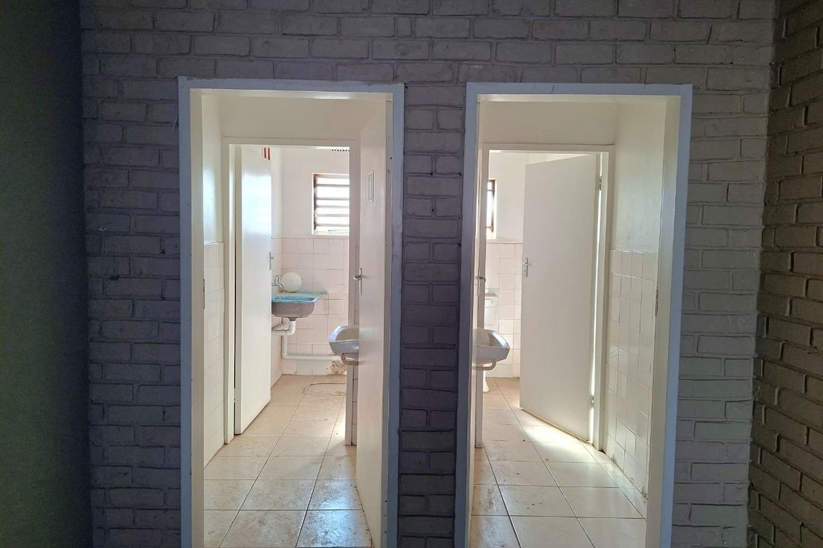 A commercial bathroom facility featuring two separate stalls with wall-mounted basins, tiled flooring, and exposed brick wall finishes.