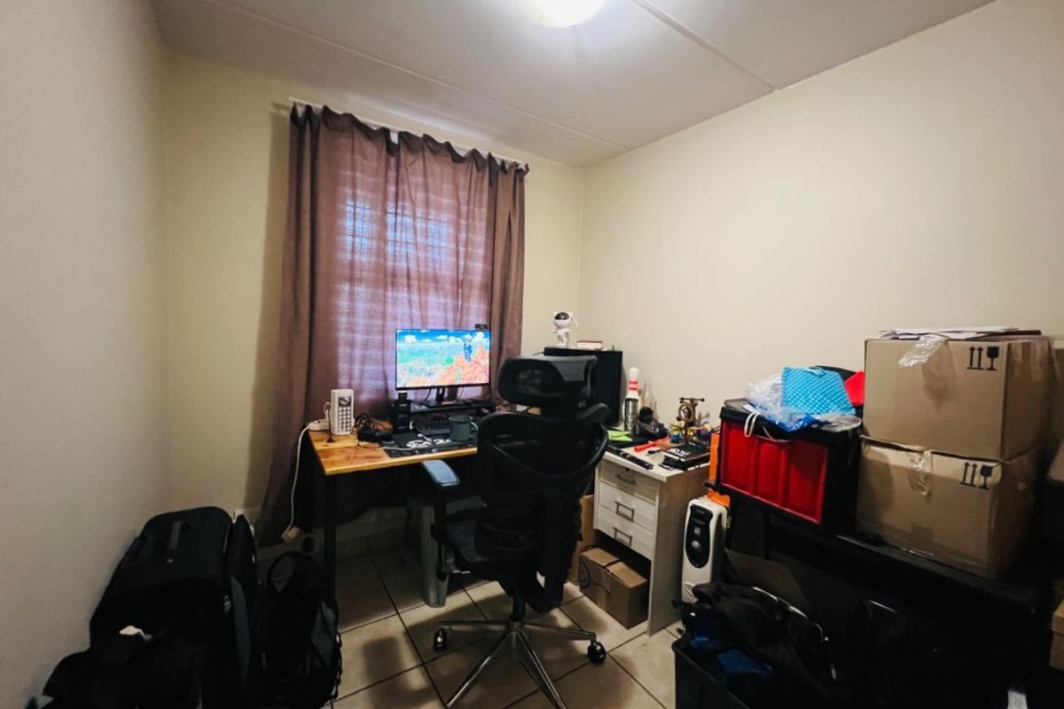 A compact bedroom featuring tiled flooring and a central ceiling light, currently utilized as a home office space.
