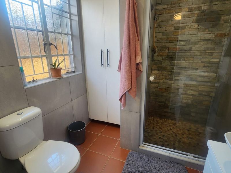 A functional bathroom featuring a shower with stone-clad walls and pebble flooring, a built-in storage cupboard, and neutral wall tiling.