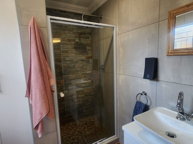 Modern bathroom featuring a glass-enclosed shower with a stone feature wall, pebble flooring, and a contemporary vanity basin with a mixer tap.