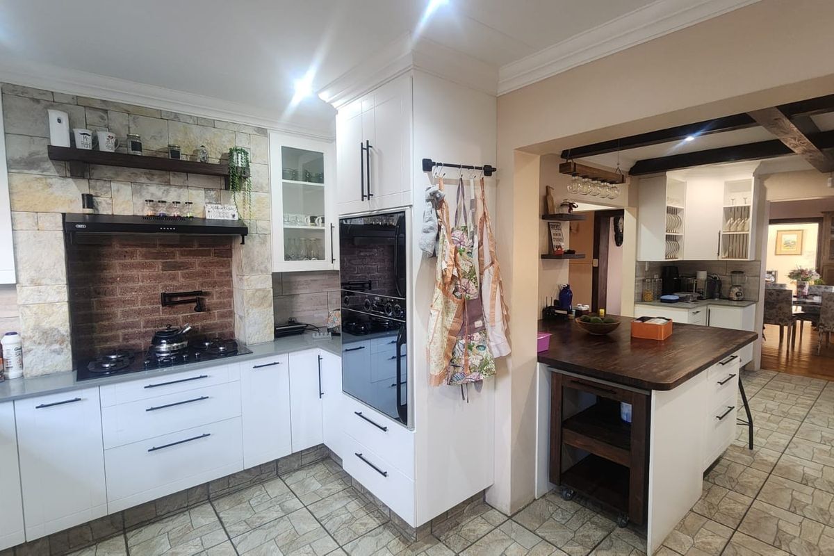 A well-appointed kitchen featuring white cabinetry, a stone-clad backsplash with exposed brick, a gas hob, built-in oven, and a central timber-topped island.
