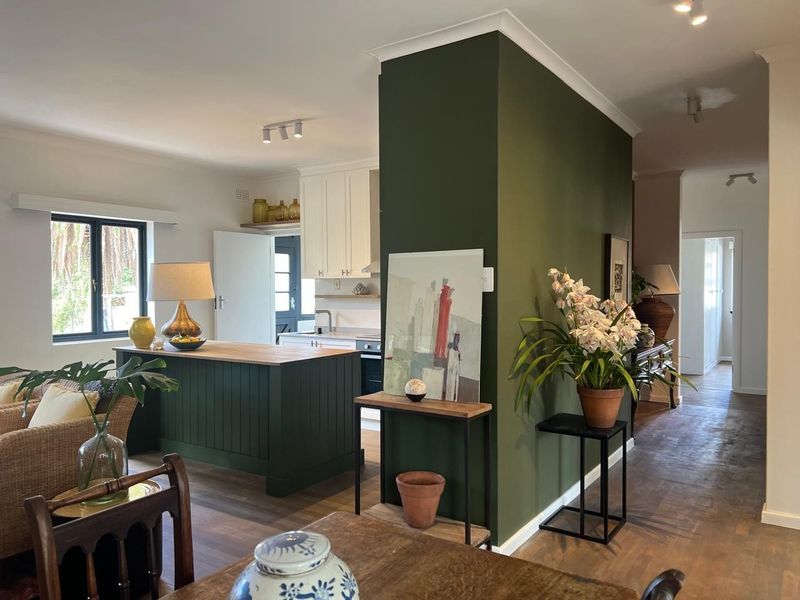 An open-plan living and kitchen area featuring a dark green kitchen island, timber flooring, and a functional kitchen layout with built-in cabinetry.