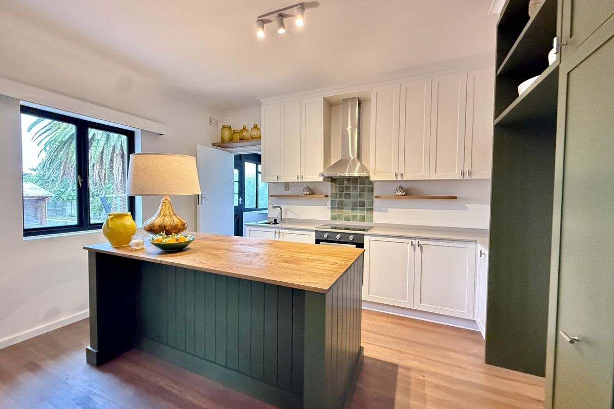 Modern kitchen featuring a dark green island with timber countertop, white cabinetry, stainless steel extractor fan, and tiled backsplash.
