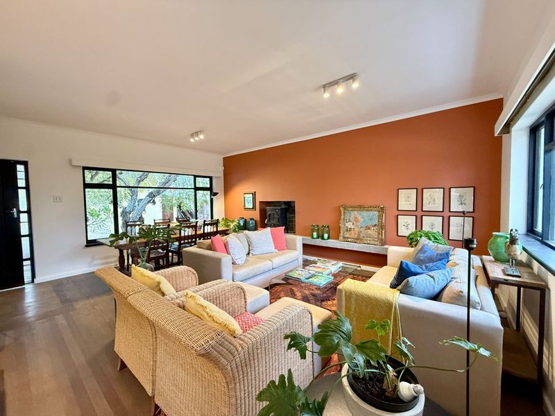Spacious open-plan living area featuring timber flooring, a wood-burning fireplace with a concrete mantel, and large windows overlooking the garden.