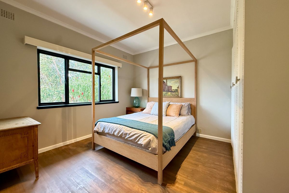 A well-maintained bedroom featuring timber flooring, neutral wall tones, a built-in wardrobe, and large windows providing natural light.