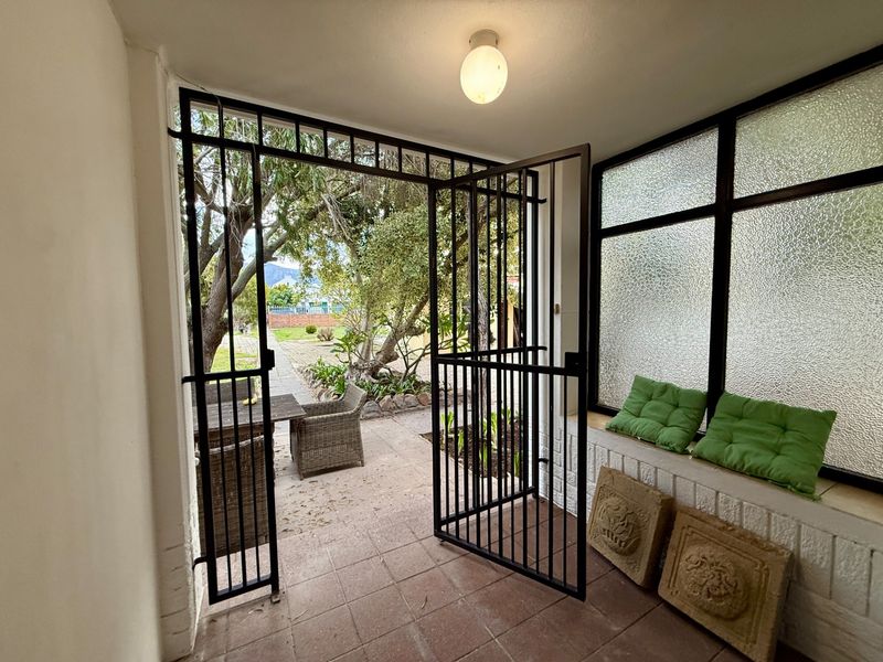 A covered patio area featuring a security gate, tiled flooring, and a built-in bench with textured glass windows overlooking the garden.