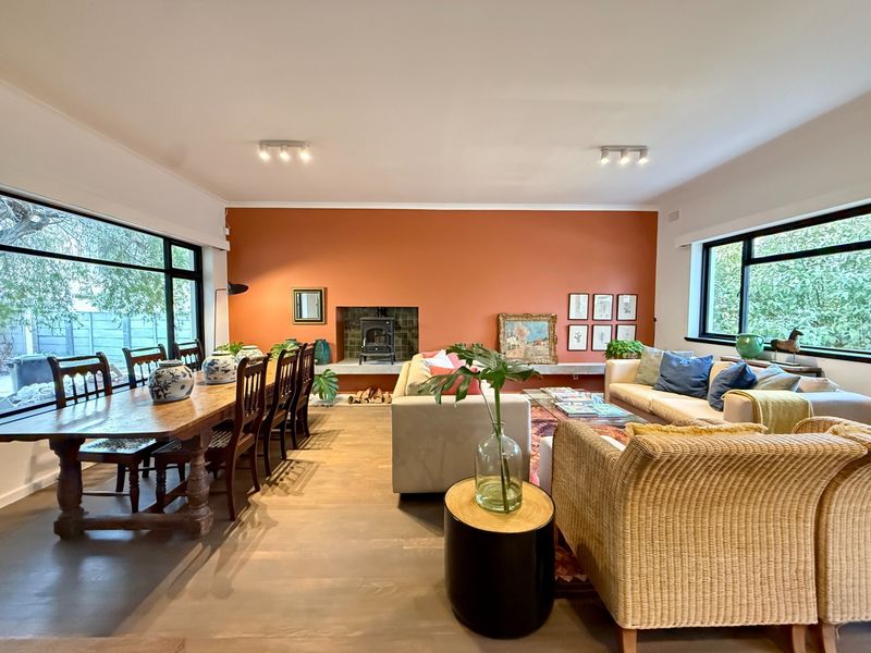 Spacious open-plan living and dining area featuring a prominent wood-burning fireplace, large windows providing natural light, and polished hardwood flooring.