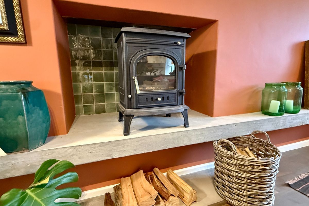 A cozy living room feature fireplace with a cast iron wood burning stove set on a concrete hearth with green tiled backing.