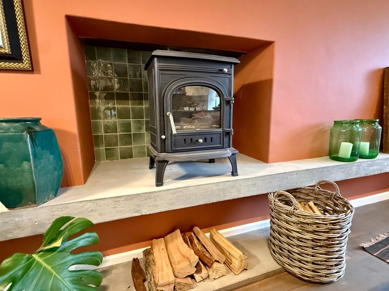 A cozy living room feature fireplace with a cast iron wood burning stove set on a concrete hearth with green tiled backing.
