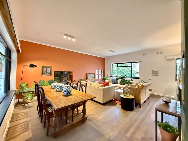 Spacious open-plan living and dining area featuring timber flooring, a built-in wood-burning fireplace, and large windows providing ample natural light.