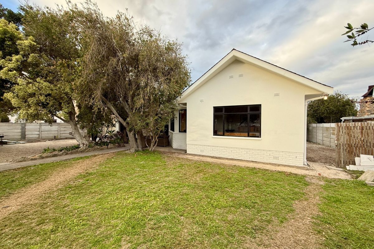 Rear view of the property featuring a painted brick facade, gabled roof, black framed windows, and a spacious garden area with boundary walls.