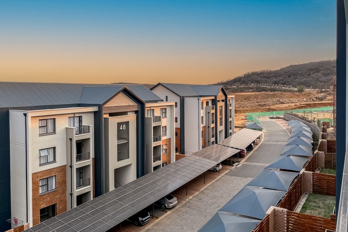 Elevated view of a modern apartment complex featuring brick and plaster facades, private balconies, and a large solar panel covered parking area.