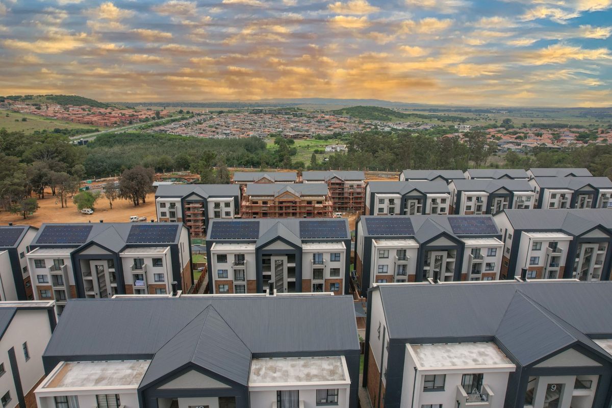 Aerial view of a modern residential apartment complex featuring multiple buildings with pitched roofs and integrated solar panels under a sunset sky.