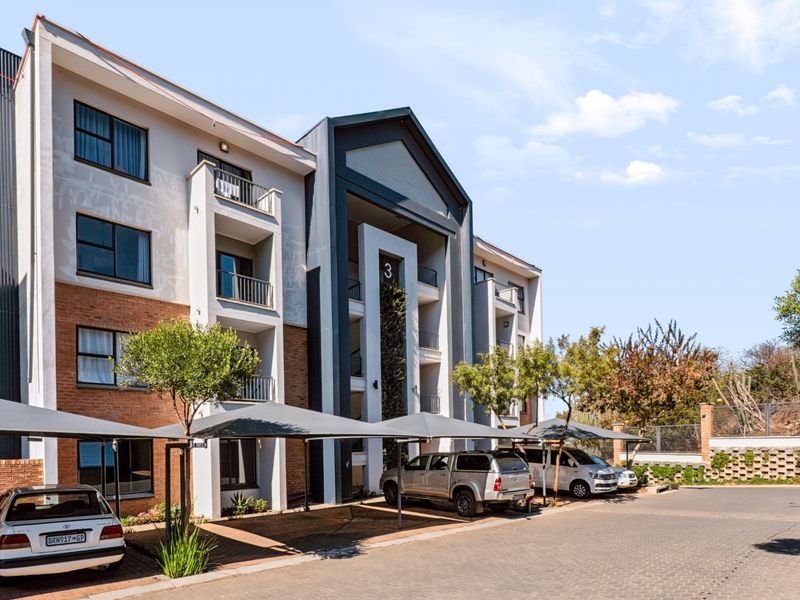 Exterior view of a multi-story apartment building featuring brick and rendered facade, private balconies, and dedicated covered parking bays.
