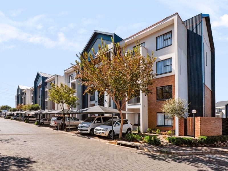 A modern apartment complex exterior featuring brick and rendered facades, aluminium windows, and covered parking bays along a paved driveway.