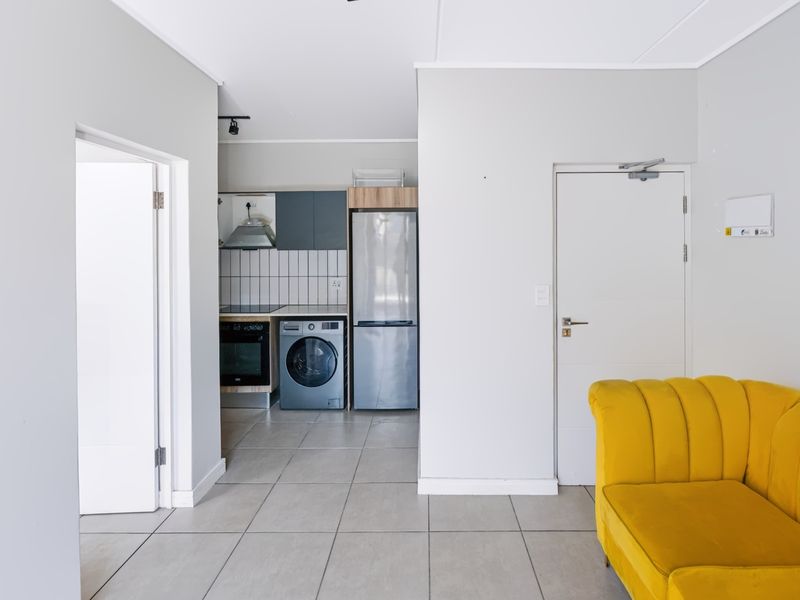 Open-plan living area featuring a compact kitchen with built-in cabinetry, oven, hob, and extractor fan, finished with neutral floor tiles.