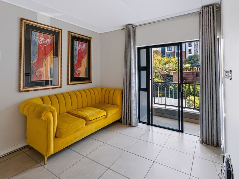 A bright living area featuring neutral tiled flooring and a sliding glass door providing direct access to a private balcony.