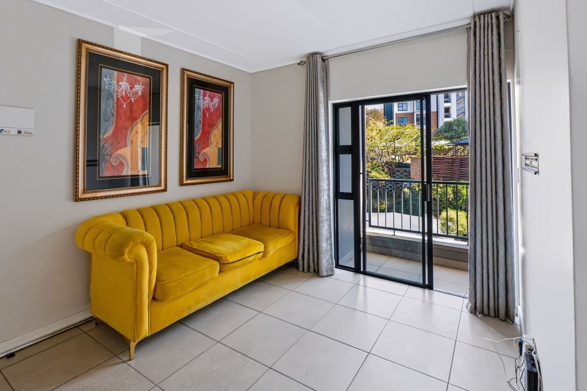 A bright living area featuring neutral tiled flooring and a sliding glass door providing direct access to a private balcony.
