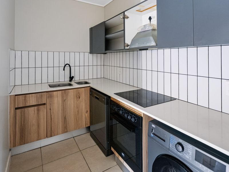 A compact kitchen featuring modern wood-grain and dark cabinetry, stone countertops, subway tile backsplash, and integrated appliances including an oven and hob.