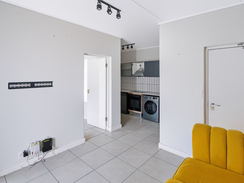 Open plan living area featuring tiled flooring, track lighting, and a compact kitchen with built-in oven and extractor fan.