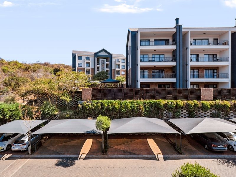 Modern apartment complex featuring multi-level residential units with private balconies and dedicated shade cloth carport parking bays.