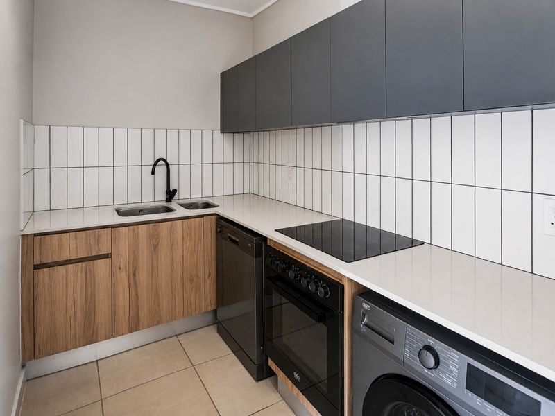 Modern kitchen featuring sleek dark grey upper cabinetry, wood-grain lower cabinets, stone countertops, subway tile backsplash, and integrated appliances.