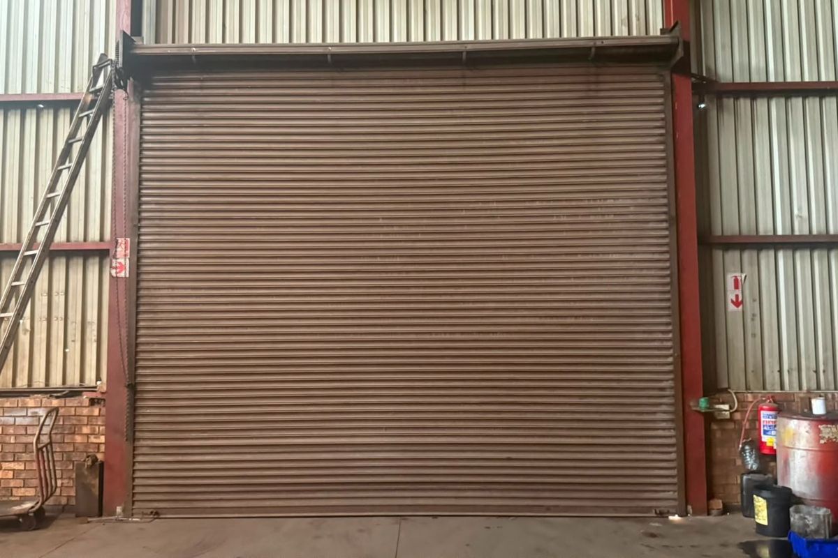 Industrial warehouse space featuring a large roller shutter door, corrugated metal wall cladding, and exposed steel structural framing.
