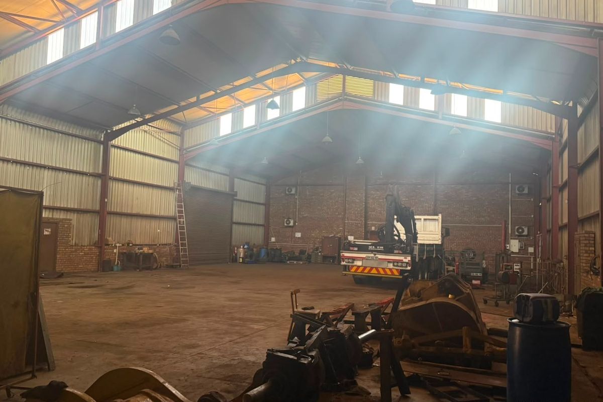 Spacious industrial warehouse featuring a high-clearance steel portal frame, exposed brick walls, large roller shutter access, and natural light through integrated skylights.